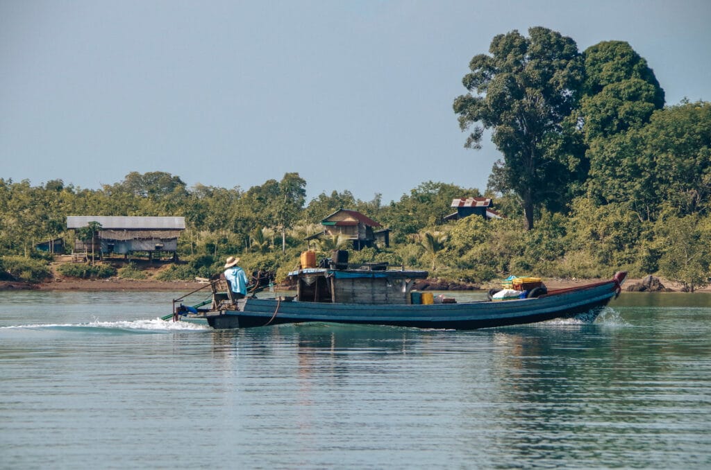 homme pilotant un bateau de pêche dans l'archipel des Mergui avec un village en toile de fond