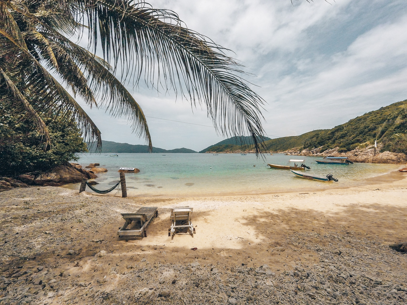 plage avec des cocotiers, transats et bateaux aux îles Perhentians