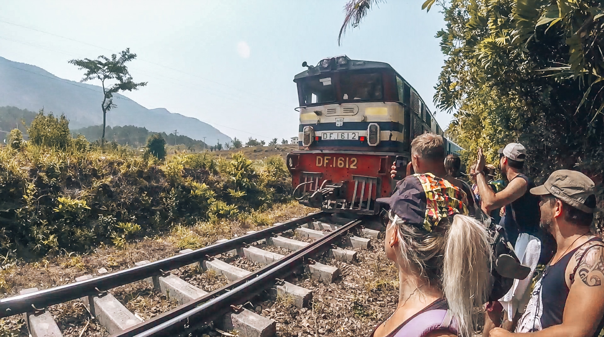 jeunes gens à côté d'une voie ferrée où passe un train très près d'eux au Myanmar